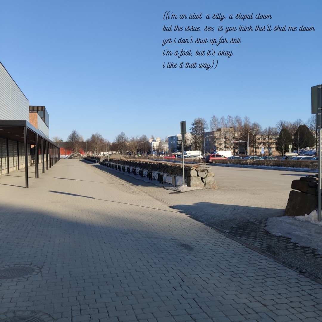 The outside of a building with a lot of cars and bikes.

A poem reads:

"((i'm an idiot, a silly, a stupid clown
but the issue, see, is you think this'll shut me down
yet i don't shut up for shit
i'm a fool, but it's okay,
i like it that way))"